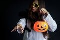 Halloween orange pumpkin in hand of beautiful attractive black long hair woman in spooky white ghost costume standing in dark room Royalty Free Stock Photo