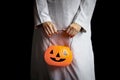 Halloween orange pumpkin in hand of woman in spooky white ghost costume standing in black dark background, female with scary Royalty Free Stock Photo