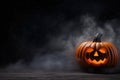 Halloween pumpkin with a scary smiling luminous face with copy space on a fog smoke dark background Royalty Free Stock Photo