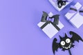 Halloween paper gift boxes with black bows and silly felt bat on side of purple background with copy space