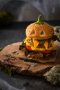 Halloween party burger in shape of scary pumpkin on a natural wooden board on dark background. Scary Halloween food concept. Royalty Free Stock Photo