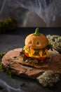 Halloween party burger in shape of scary pumpkin on a natural wooden board on dark background. Scary Halloween food concept. Royalty Free Stock Photo