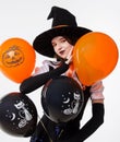 Halloween Party girl. Beautiful woman in black witch hat holding orange balloons and smiling, Studio portrait on white background Royalty Free Stock Photo