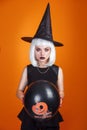 Halloween Party. Sexy witch with white hair holding black and orange Air balloon with pumpkin on orange background Royalty Free Stock Photo