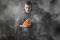 Halloween portrait Caucasian white man holding pumpkin dressed and makeup stylised for vampire on dark smoky background Royalty Free Stock Photo