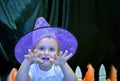 Halloween portrait of little girl wearing purple witch hat scaring the audience against black backgorund. Kid`s custom