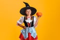 Halloween. Portrait of a little girl in a witch costume holding a pumpkin. Child in the studio on a yellow background Royalty Free Stock Photo