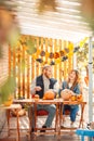 Halloween Preparaton Concept. Young couple sitting at table outdoors making jack-o`-lantern laughing playful
