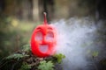 Halloween pumpkin in the autumn forest on an old stump. Jack lantern with steam from the mouth. In smoke or fog. Smoking or vaping