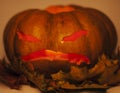 Halloween pumpkin with autumn yellow dry leafes, scary angry face close up