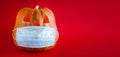 Halloween pumpkin in a protective medical mask on a red background. Copy space Royalty Free Stock Photo