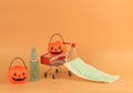 Halloween pumpkin on shopping cart with medical face mask and alcohol hand spray on orange background with copy space. Covid19