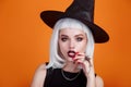 Halloween sexy witch portrait with dark lips and white hair on orange background.