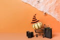 Halloween shopping holiday concept, pumpkin in grocery cart with black paper bags on orange background with spider web Royalty Free Stock Photo