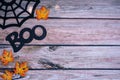 Halloween spider web, boo word phrase and maple leaves on wooden backdrop