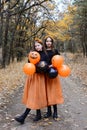 Halloween style. Two girls in traditional black-orange colors with balloons on the background of the autumn forest. Vertical