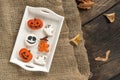 Halloween sweets lie in a wooden tray. Orange gingerbread in pumpkin shape and ghosts. Tasty cookie on table. Top view