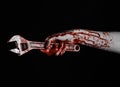 Halloween theme: bloody hand holding a big wrench on a black background Royalty Free Stock Photo