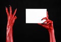 Halloween theme: Red devil hand with black nails holding a blank white card on a black background Royalty Free Stock Photo
