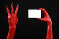 Halloween theme: Red devil hand with black nails holding a blank white card on a black background Royalty Free Stock Photo