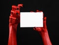 Halloween theme: Red devil hand with black nails holding a blank white card on a black background Royalty Free Stock Photo