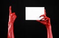 Halloween theme: Red devil hand with black nails holding a blank white card on a black background Royalty Free Stock Photo