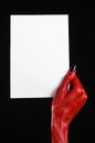 Halloween theme: Red devil hand with black nails holding a blank white card on a black background Royalty Free Stock Photo