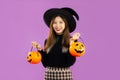 Halloween theme, young asian woman in black costume wearing witch hat smiling and holding pumpkin lantern on purple backgroud Royalty Free Stock Photo