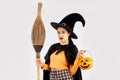 Halloween theme, young asian woman in witch costume holding broom and carrying orange pumpkin bucket lantern posing on white Royalty Free Stock Photo