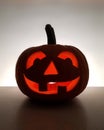 Halloween traditional smiling jack-o-lantern vertical image. Carved glowing pumpkin, blurred back wall is highlighted white.