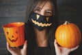 Halloween 2020 trick or treat. Woman in evil face mask holding pumpkin and jack o lantern pail