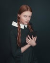 Halloween vampire woman looks directly into the camera holding book. Female portrait in vintage style on dark background. Royalty Free Stock Photo