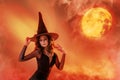 Halloween witch. A beautiful young woman in a witch`s hat conjures, practices witchcraft against the backdrop of a sunset. Wide Royalty Free Stock Photo