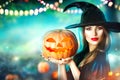 Halloween witch with a carved pumpkin and magic lights in a forest