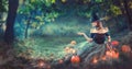 Halloween Witch with a carved pumpkin and magic lights in a dark forest at night. Beautiful young woman in witches costume Royalty Free Stock Photo