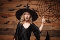 Halloween Witch concept - closeup shot of little caucasian witch child shocking face posing with bat and spider web on wooden stud