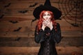 Halloween witch concept - Happy Halloween red hair Witch holding posing with shocked face over old wooden studio background. Royalty Free Stock Photo