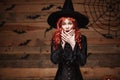 Halloween witch concept - Happy Halloween red hair Witch holding posing with shocked face over old wooden studio background. Royalty Free Stock Photo