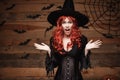 Halloween witch concept - Happy Halloween red hair Witch holding posing with shocked face over old wooden studio background. Royalty Free Stock Photo