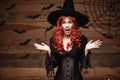 Halloween witch concept - Happy Halloween red hair Witch holding posing with shocked face over old wooden studio Royalty Free Stock Photo