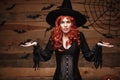 Halloween witch concept - Happy Halloween red hair Witch holding posing with shocked face over old wooden studio Royalty Free Stock Photo