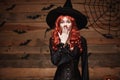 Halloween witch concept - Happy Halloween red hair Witch holding posing with shocked face over old wooden studio background. Royalty Free Stock Photo