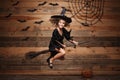 Halloween Witch concept - little caucasian witch child flying on magic broomstick over bat and spider web background. Royalty Free Stock Photo