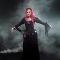 Halloween Witch creates magic. Attractive woman with red hair in witches costume standing outstretched arms, strong wind