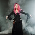 Halloween Witch creates magic. Attractive woman with red hair in witches costume standing outstretched arms, strong wind