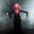 Halloween Witch creates magic. Attractive woman with red hair in witches costume standing outstretched arms, strong wind