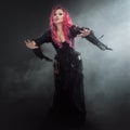 Halloween Witch creates magic. Attractive woman with red hair in witches costume standing outstretched arms, strong wind