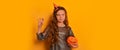 Halloween witch girl with Halloween pumpkin, showing Boo and looking at camera on yellow background with copy space.