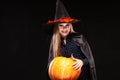 Halloween Witch with Pumpkin on black background. Beautiful young surprised woman in witches hat and costume holding Royalty Free Stock Photo