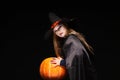 Halloween Witch with Pumpkin on black background. Beautiful young surprised woman in witches hat and costume holding Royalty Free Stock Photo